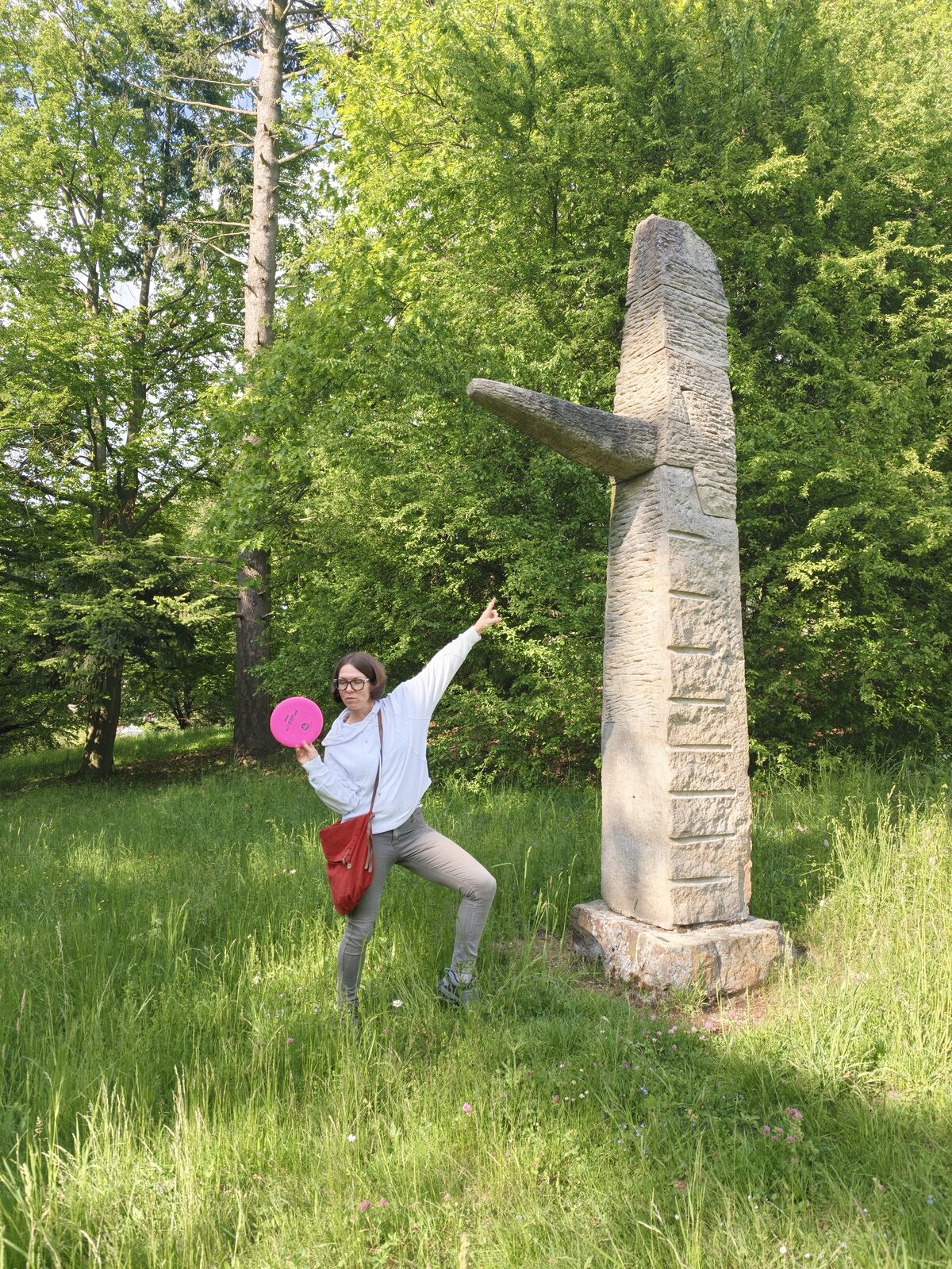 Hráčka hází disk vedle vysoké pískovcové sochy – směrem pryč od ní